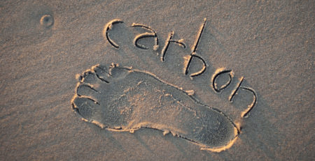 Eco-friendly carbon footprint message handwritten with the outline of a foot on a grainy golden sand beach