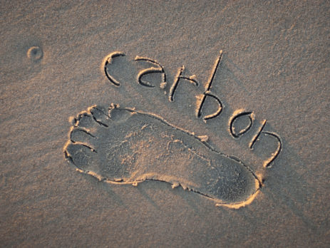 Eco-friendly carbon footprint message handwritten with the outline of a foot on a grainy golden sand beach