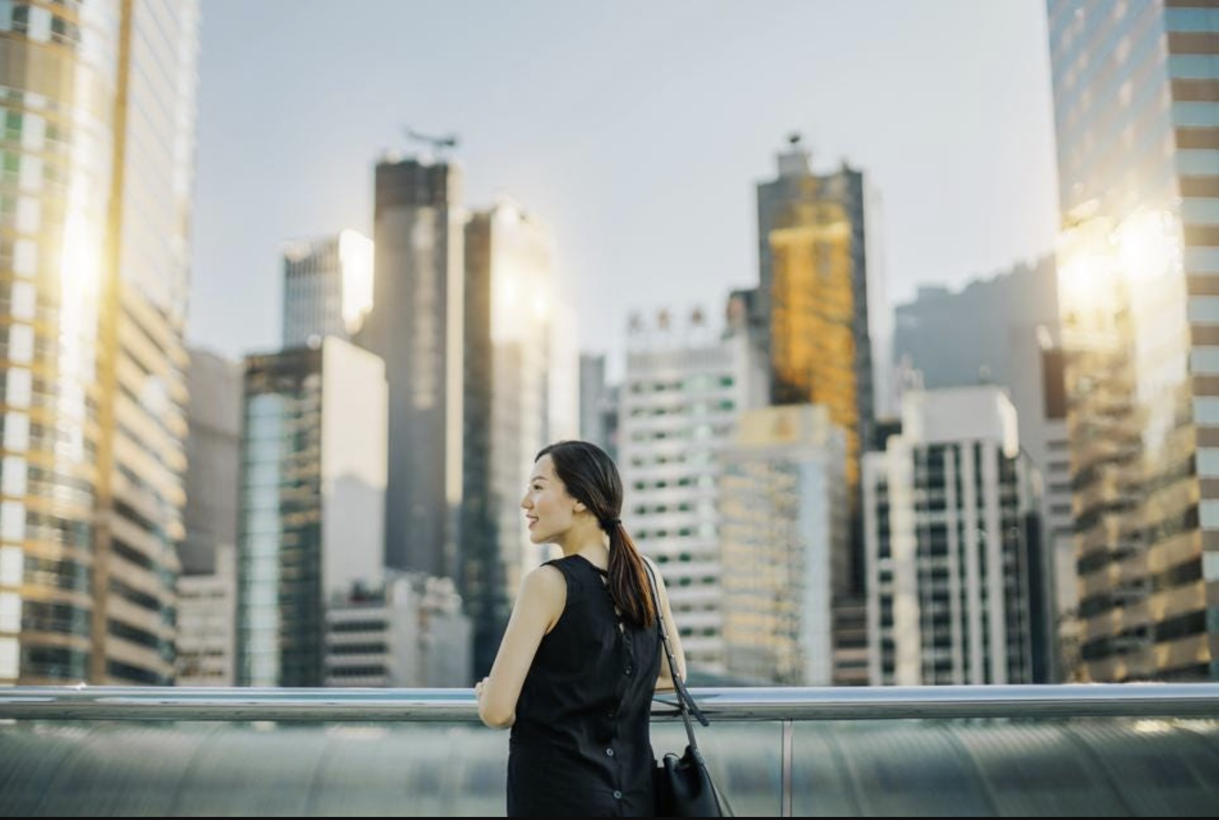 Beautiful young Asian woman enjoying the city view during sunset on urban balcony